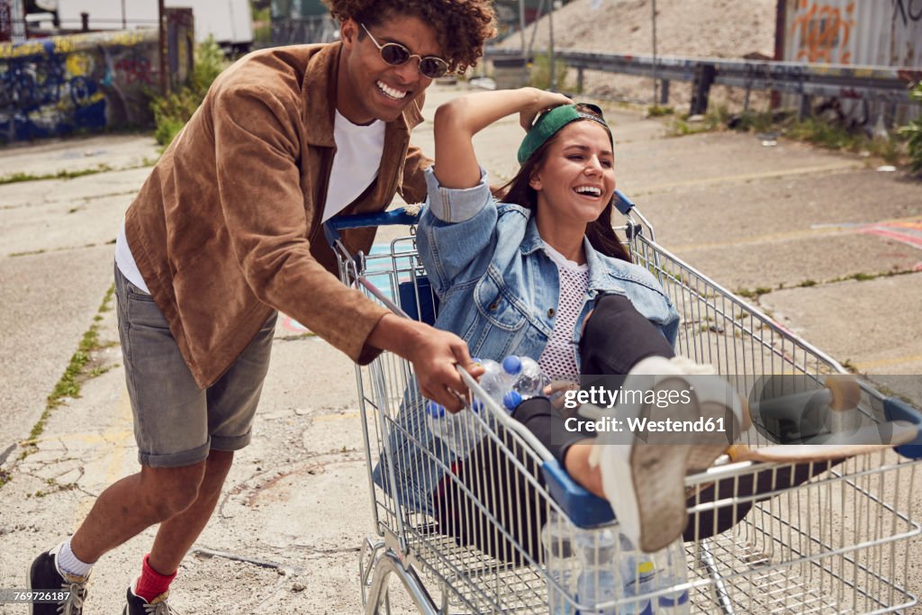 Young man pushing girlfriend sitting in shopping cart