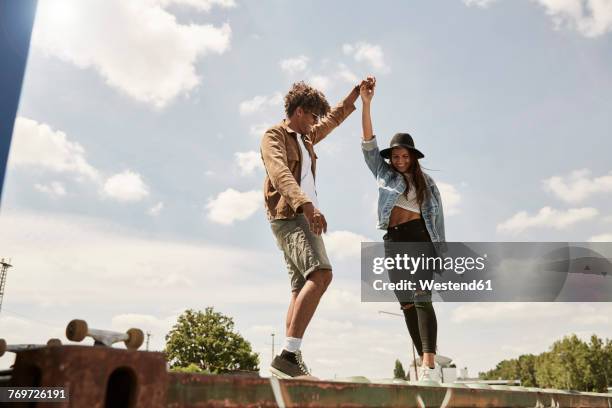 young couple standing on wall, raising arms - young man arms up stock-fotos und bilder