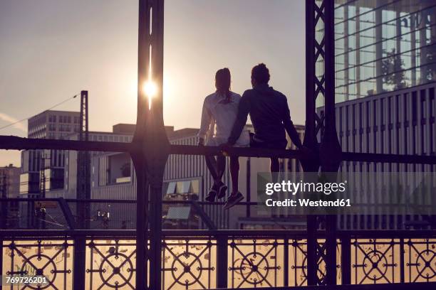 germany, munich, young couple sitting on bridge, enjoying sunset - silhouette münchen stock pictures, royalty-free photos & images