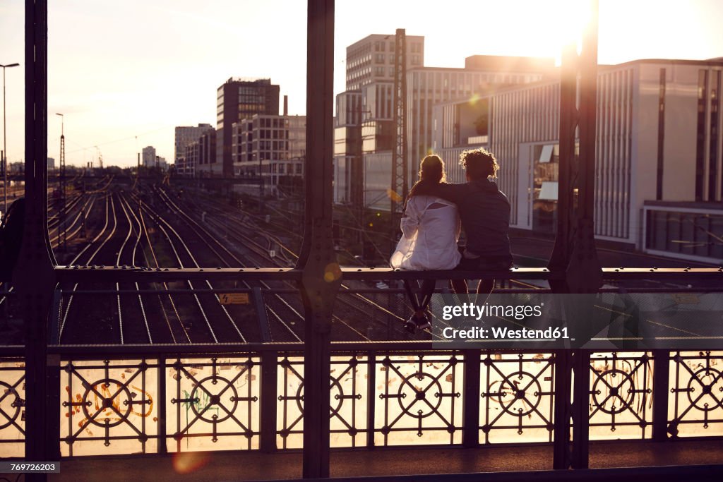 Germany, Munich, Young couple sitting on bridge, enjoying sunset