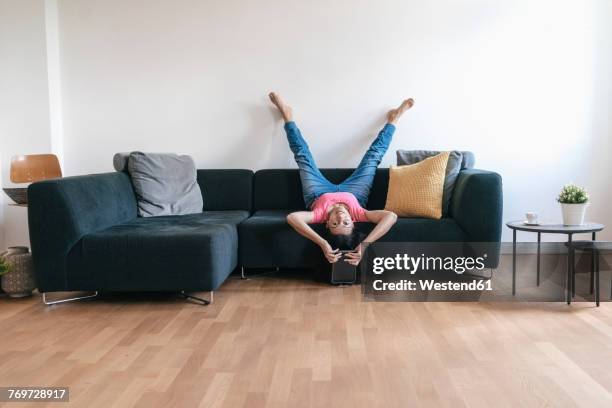 woman at home with tablet lying on sofa upside down - piernas en el aire fotografías e imágenes de stock