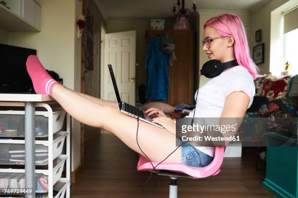 young woman with pink hair wearing headphones and using laptop at home - pink sock image stock pictures, royalty-free photos & images
