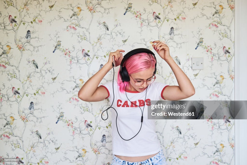 Enthusiastic young woman with pink hair listening to music at home