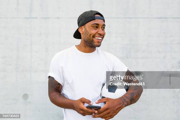 portrait of laughing young man with soccer ball and cell phone - sideways glance stock pictures, royalty-free photos & images