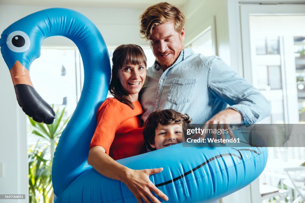 Happy parents with son holding an inflatable flamingo at home