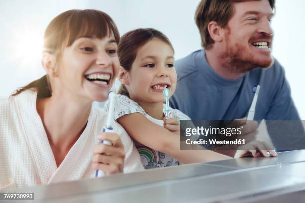 family of three brushing their teeth in front of big mirror - mouth hygiene brush stock pictures, royalty-free photos & images