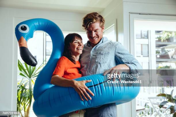 happy couple holding an inflatable flamingo at home - konzepte und themen stock-fotos und bilder