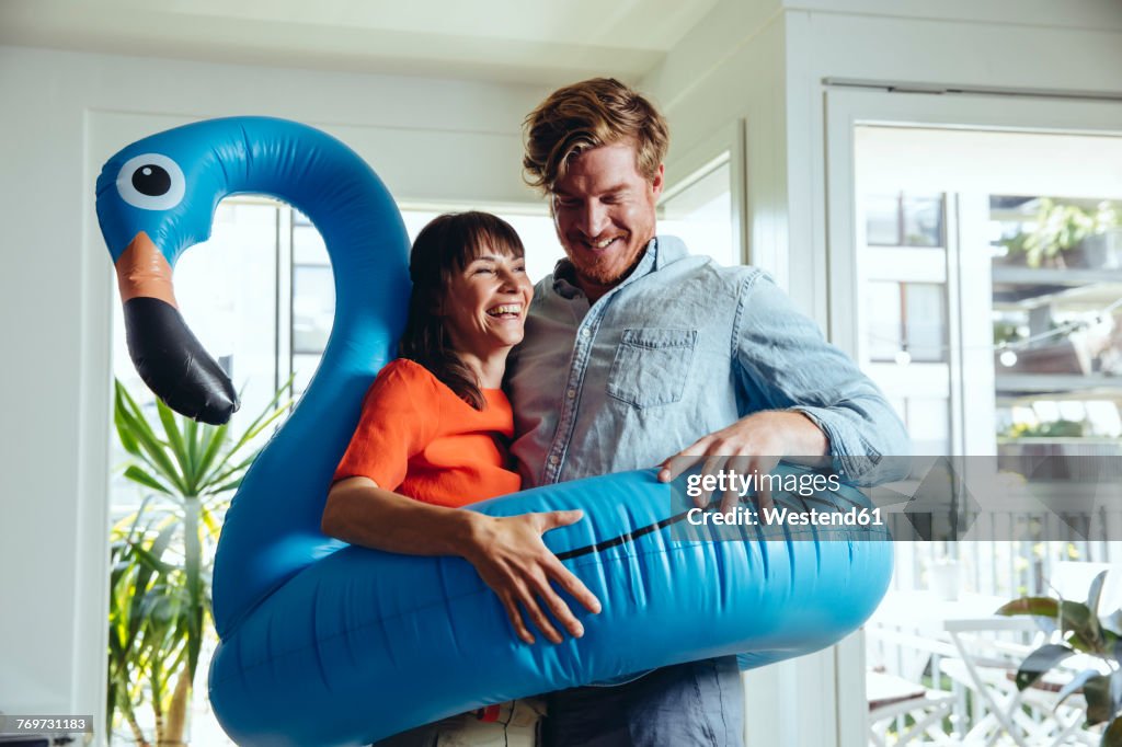 Happy couple holding an inflatable flamingo at home