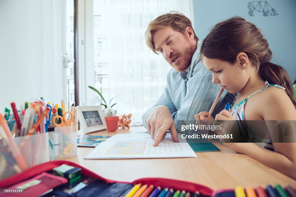 Father helping girl doing her schoolwork at home