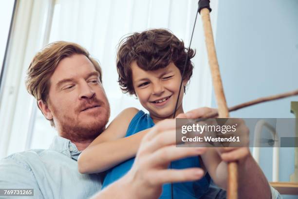 father showing son how to use self-made bow and arrow - pfeil und bogen stock-fotos und bilder