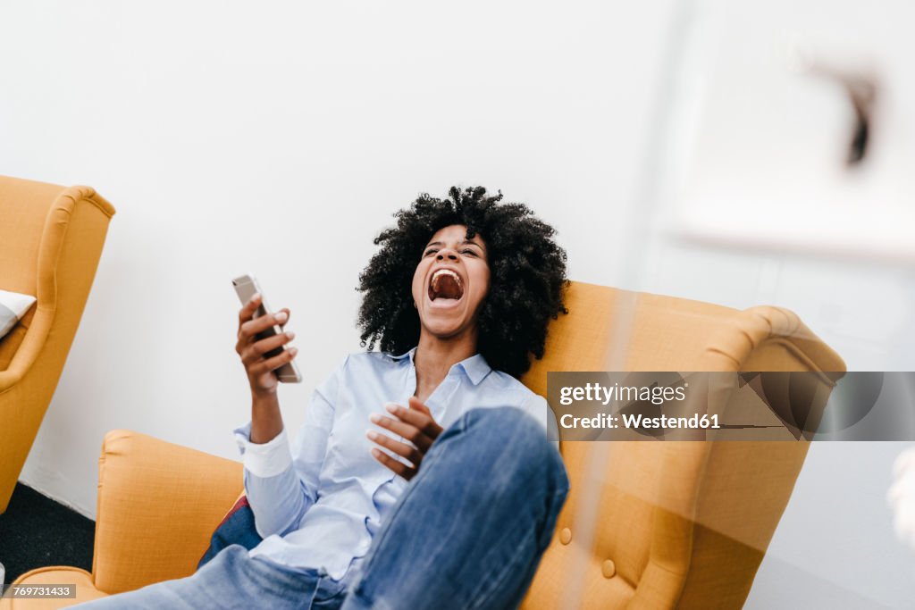 Screaming young woman with cell phone sitting in armchair