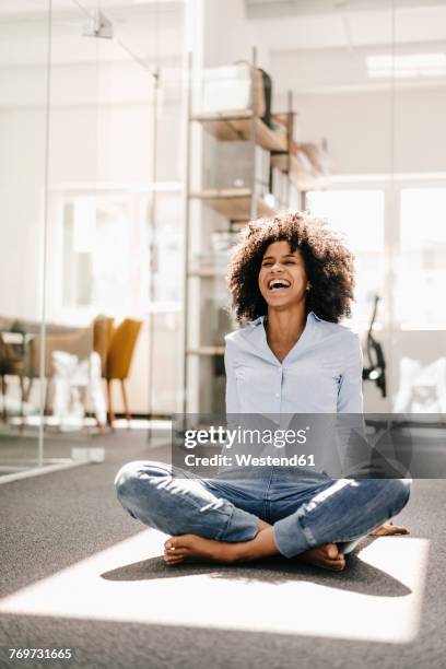 happy young woman sitting on floor in office - cross legged stock pictures, royalty-free photos & images