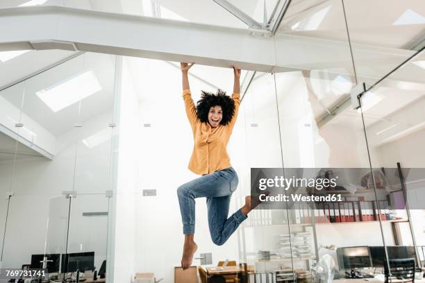 happy young woman hanging on beam in office - sport extreme stock-fotos und bilder