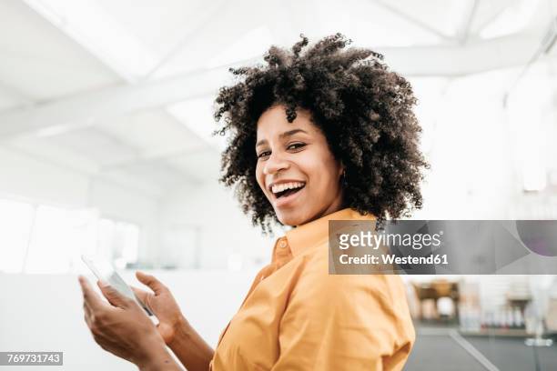 portrait of happy young woman holding cell phone in office - auslachen blick in die kamera stock-fotos und bilder