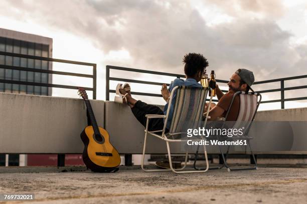 young couple with beer and guitar sitting on rooftop - positive emotionen stock-fotos und bilder