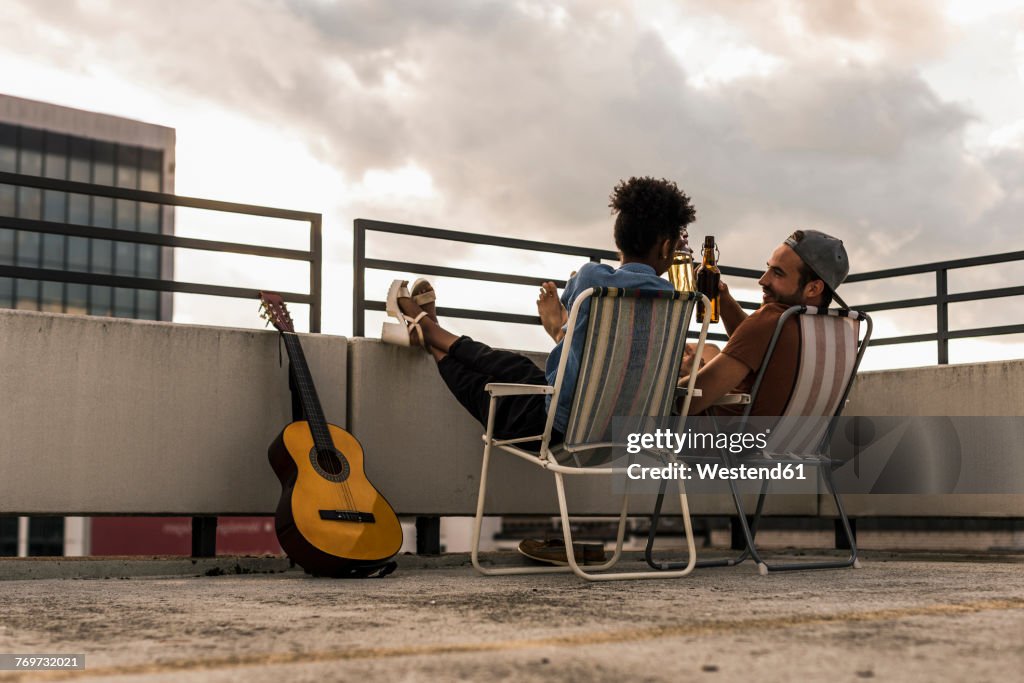 Young couple with beer and guitar sitting on rooftop
