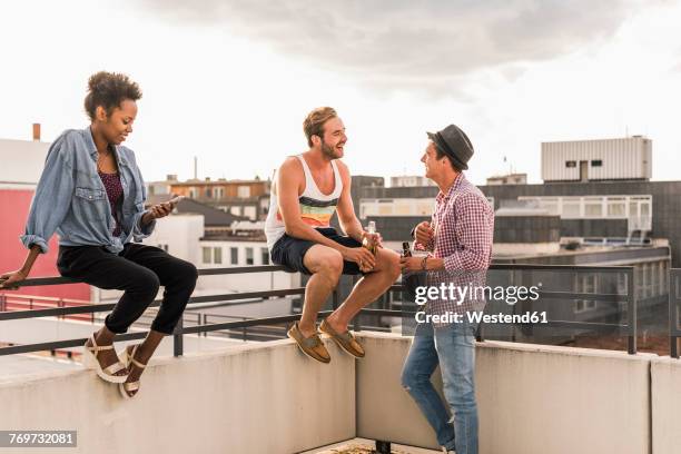 three friends socializing on a rooftop party - dachterrasse stock-fotos und bilder