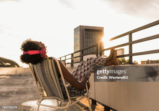 young woman with headphones sitting on rooftop - rooftop stock-fotos und bilder