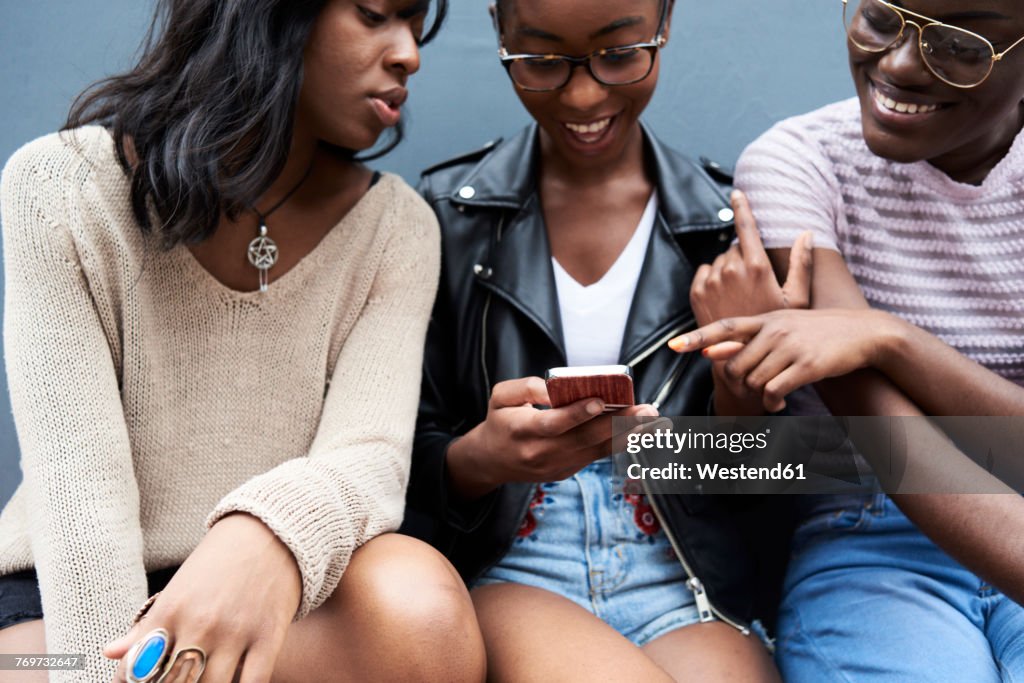 Three friends sitting side by side looking at cell phone