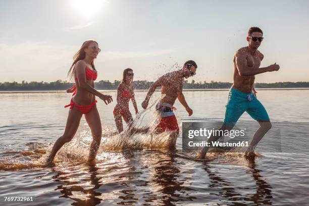 happy friends splashing in water - bathing in sunset stockfoto's en -beelden