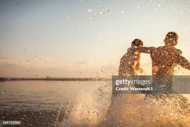 two friends running in water - bathing in sunset stockfoto's en -beelden