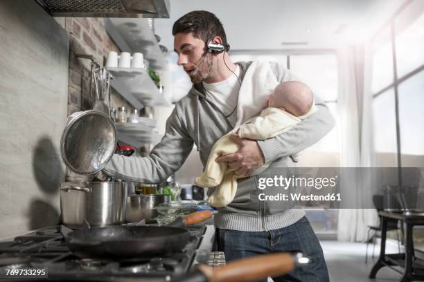 father with headset cooking in kitchen holding baby - multi tasking stock pictures, royalty-free photos & images