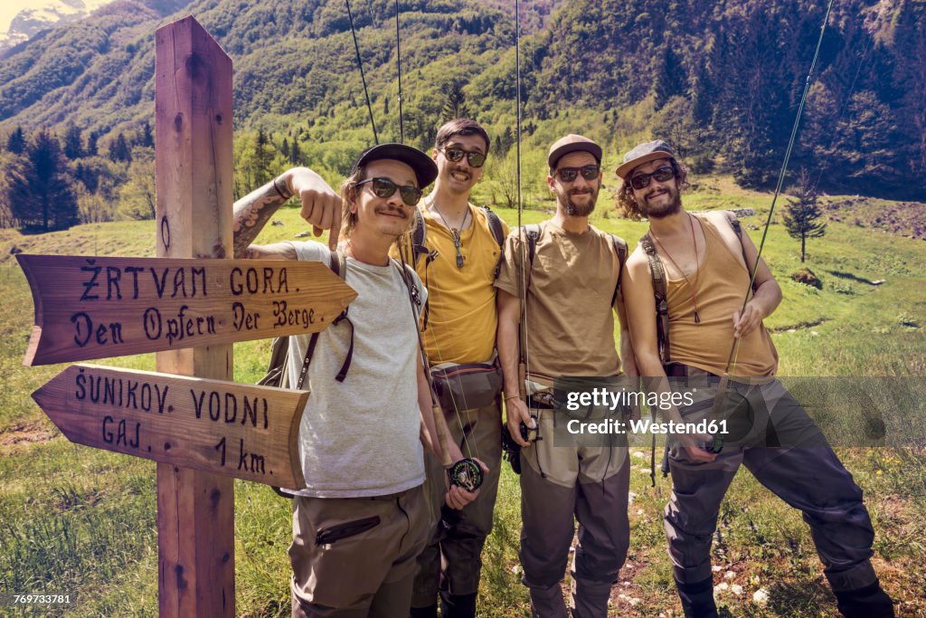 Slovenia, Bovec, four anglers posing at signpost on meadow near Soca river