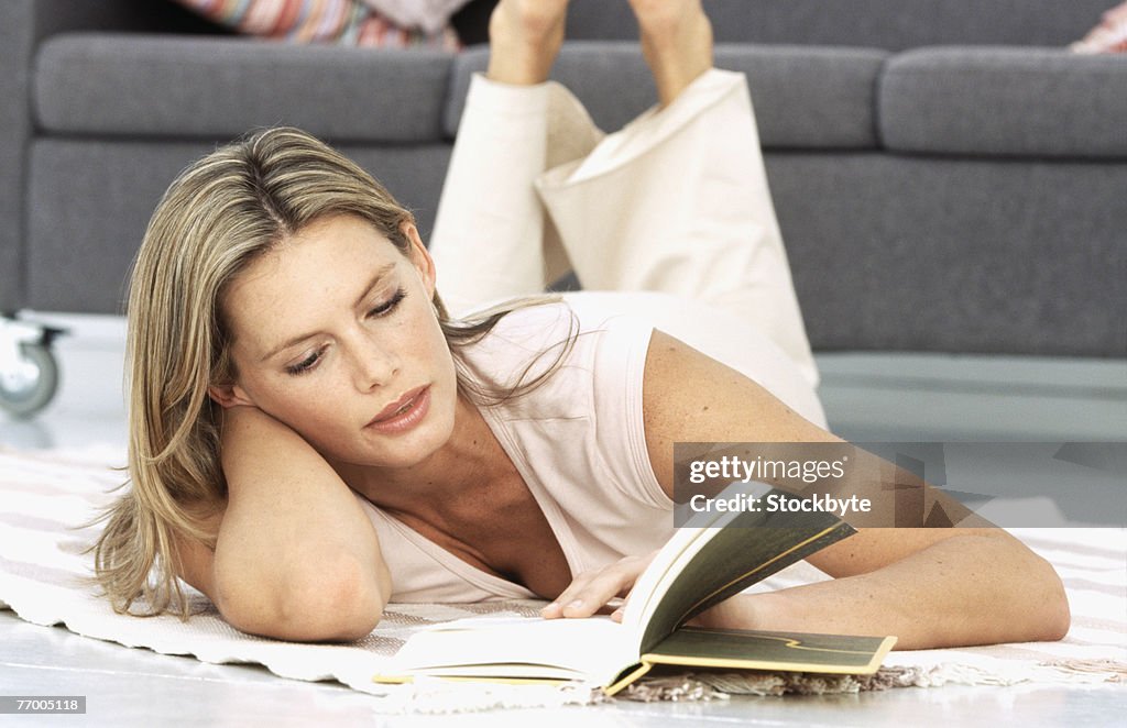 Woman lying on carpet in living room, reading book