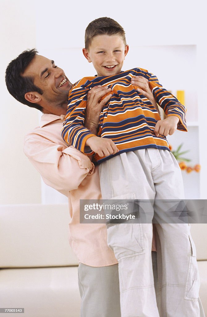 Father lifting son (10-11) in room, smiling