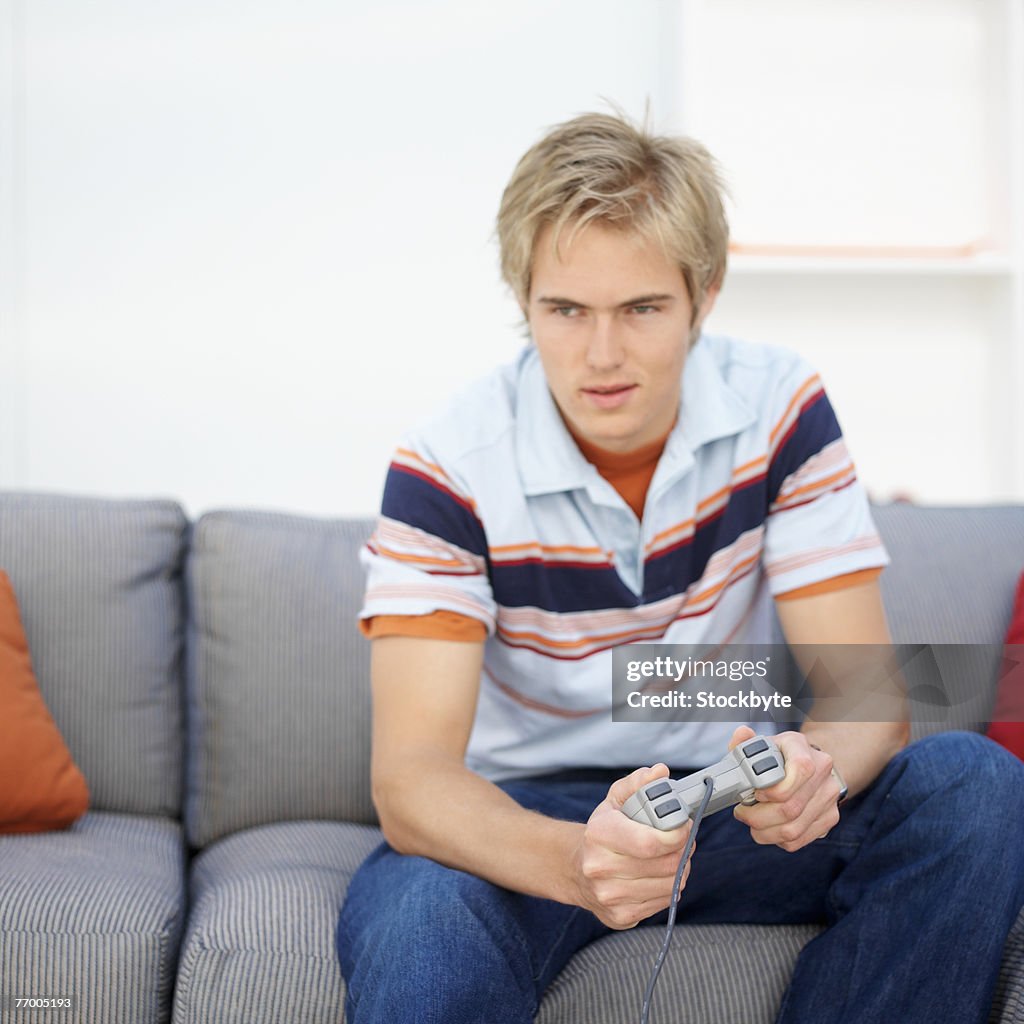 Teenage boy sitting on sofa, playing video game