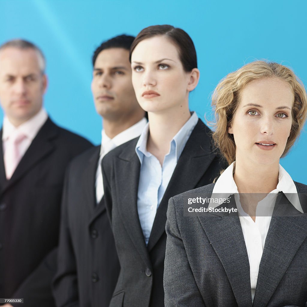 Four business people standing in row, focus on woman in foreground looking at camera