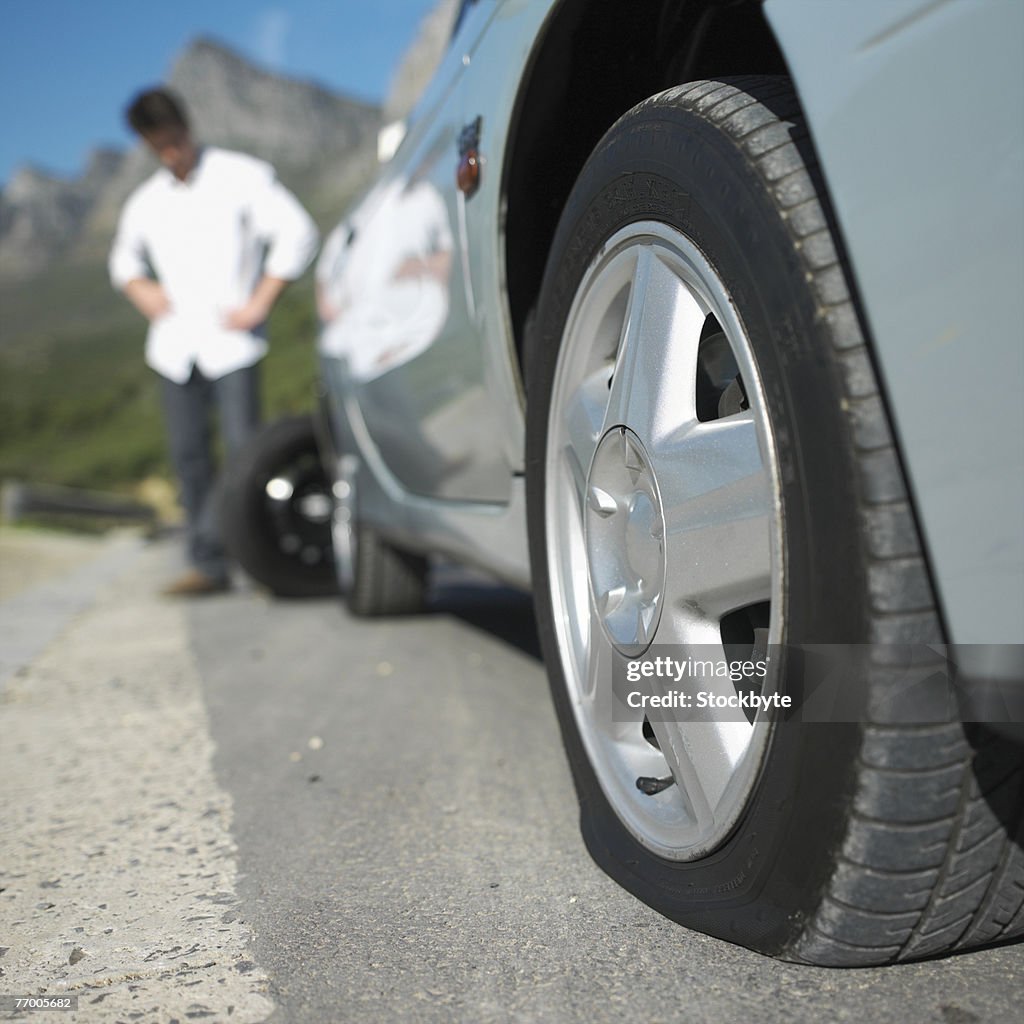 Man standing by car with flat tire, focus on tire