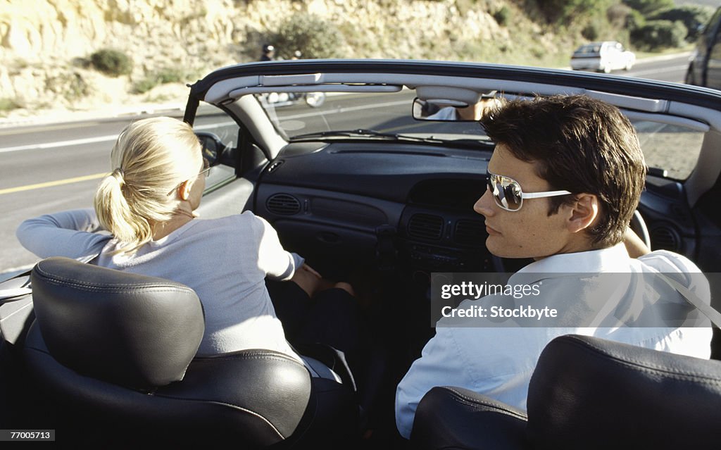 Couple in convertible car at side of road, rear view