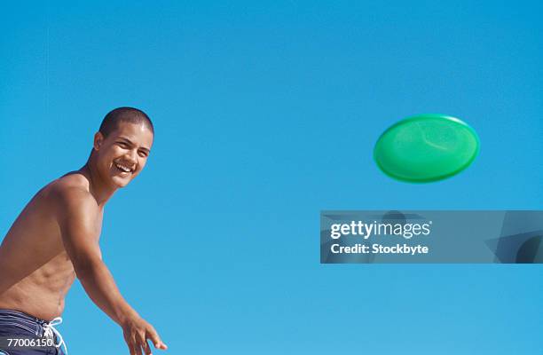 young man throwing flying disc against clear sky, upper half - half shaved hair stockfoto's en -beelden