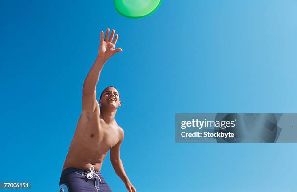 young man throwing flying disc against clear sky, upper half, low angle view - half shaved hair stockfoto's en -beelden