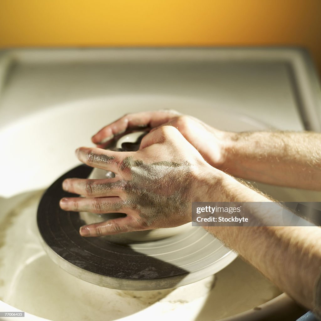 Potter working with clay on wheel, close-up of hands