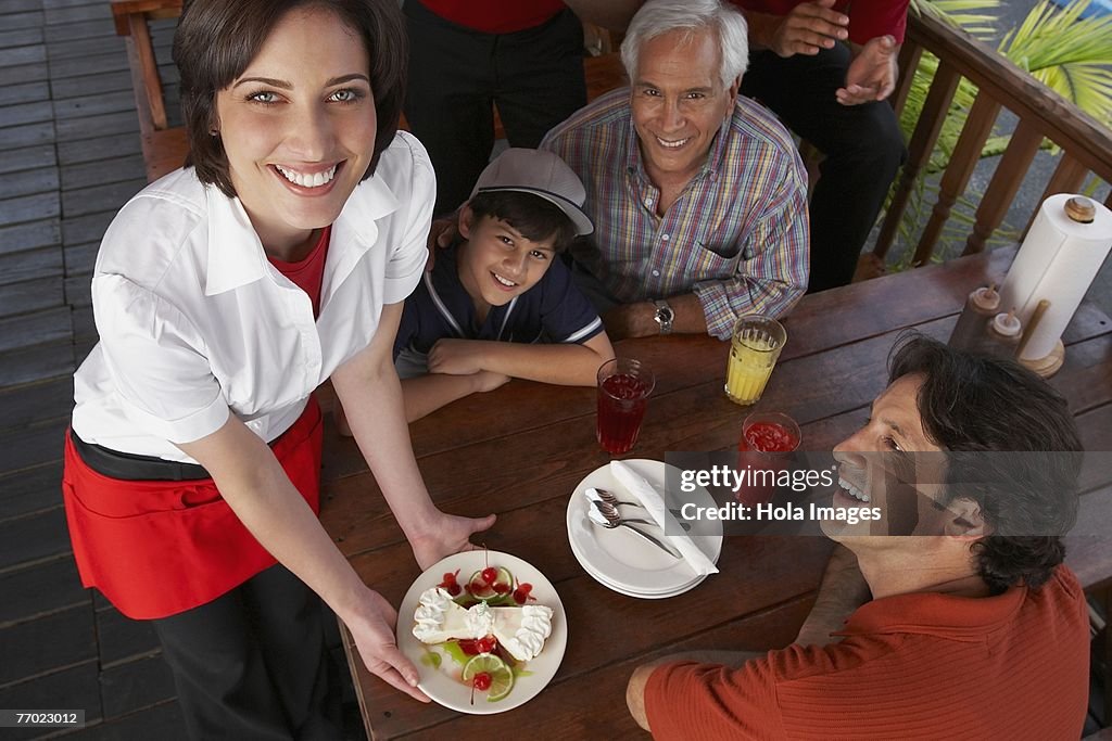 Portrait of a young woman serving dessert to a mid adult man celebrating his son's birthday in a restaurant