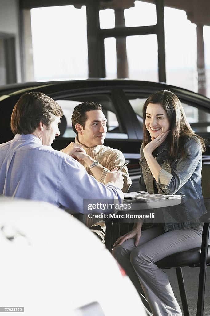 Rear view of a salesman giving details about a car to a couple in a car showroom