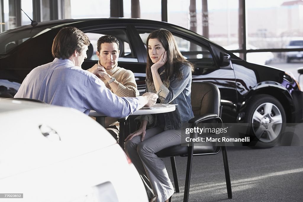 Rear view of a salesman giving details about a car to a couple in a car showroom