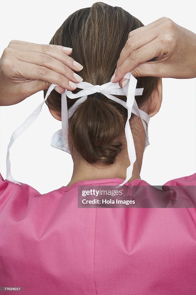 Rear view of a female nurse tying a surgical mask