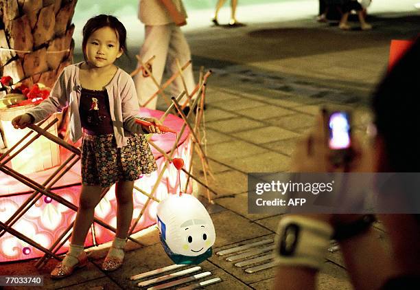 Young girl poses for a picture next to illuminations while holding a small lantern during the annual Mid-Autumn Festival at Victoria Park in Hong...