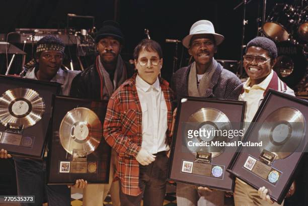 American singer-songwriter Paul Simon of folk rock duo Simon & Garfunkel posed with four musicians, all holding gold discs of Paul Simon's album...