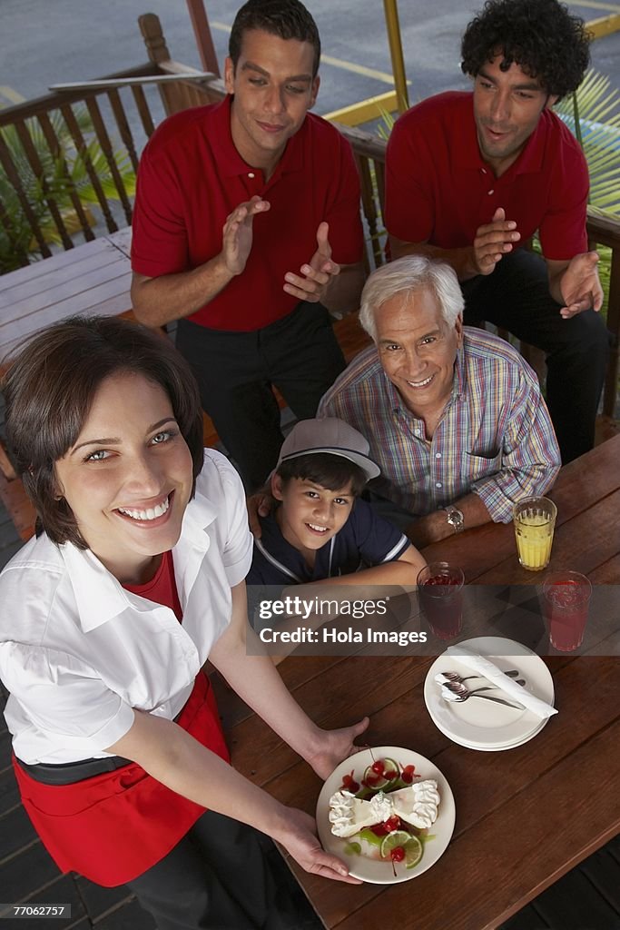 Portrait of a young woman serving dessert to a boy celebrating his birthday in a restaurant