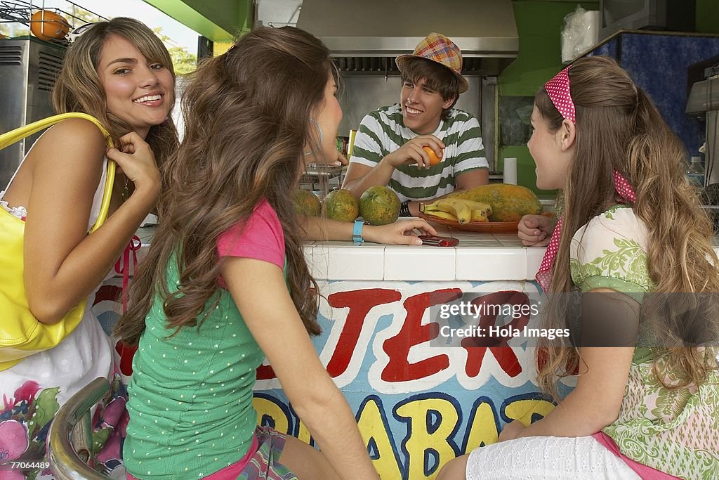 Two teenage girls talking with a bartender with another teenage girl standing beside them in a juice bar