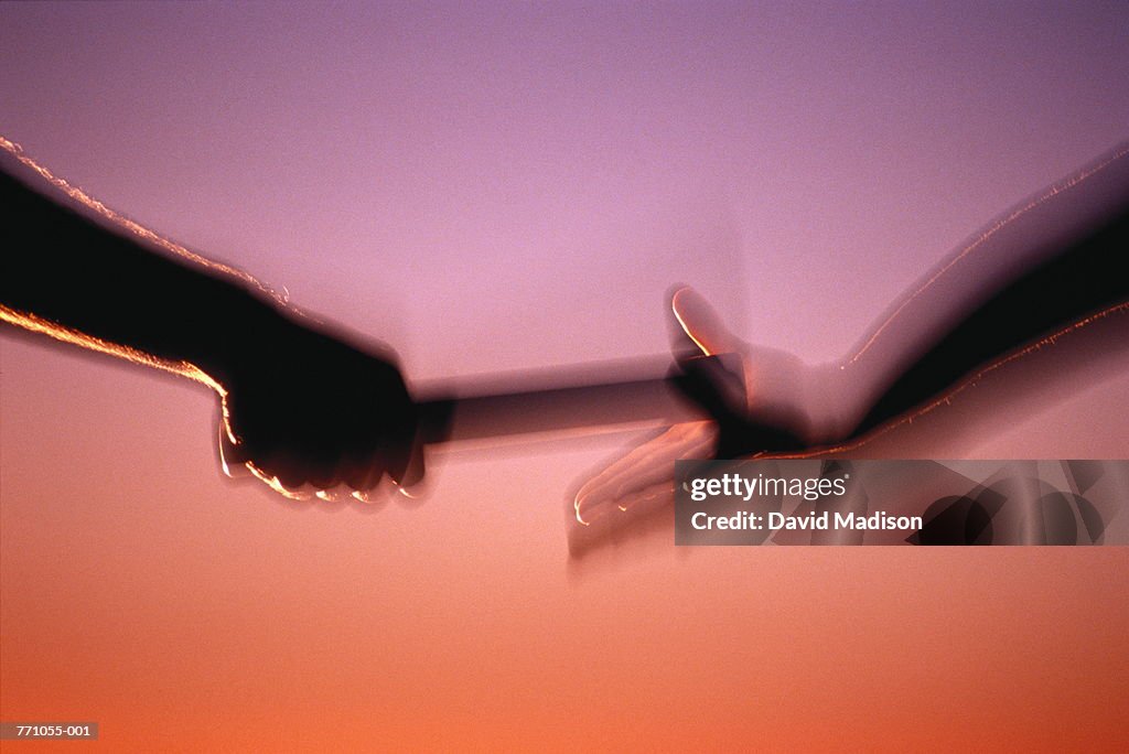 Relay runners passing baton, close-up (blurred motion)