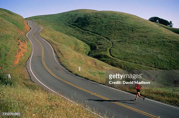 man in shorts running on country road - road running stock pictures, royalty-free photos & images