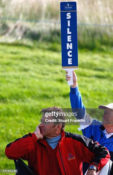 Captain Nick Faldo of The Great Britian and Ireland team looks on beside a member of staff holding up a silence sign, during the final day singles at...