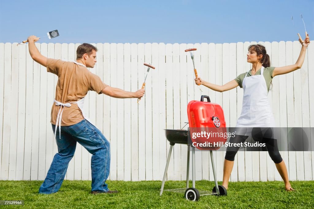 Multi-ethnic couple in fighting stance with barbeque utensils