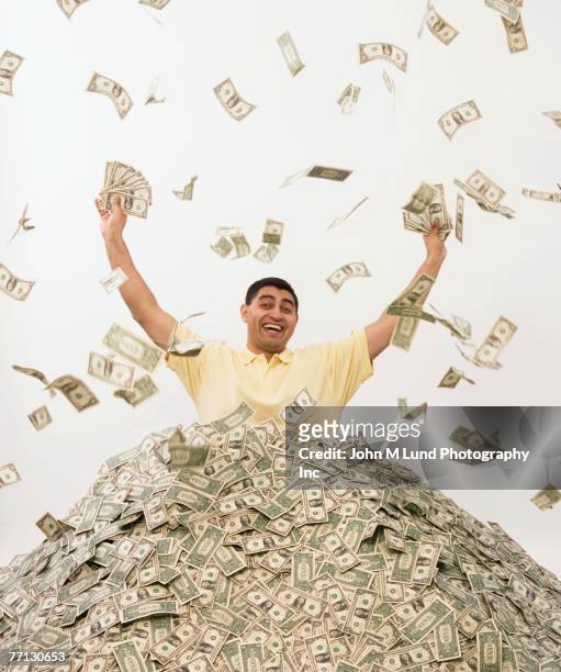 hispanic man standing in pile of money - millionnaire stock pictures, royalty-free photos & images