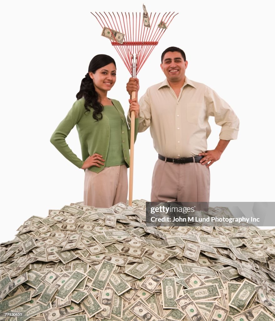 Hispanic couple standing in pile of money with rake